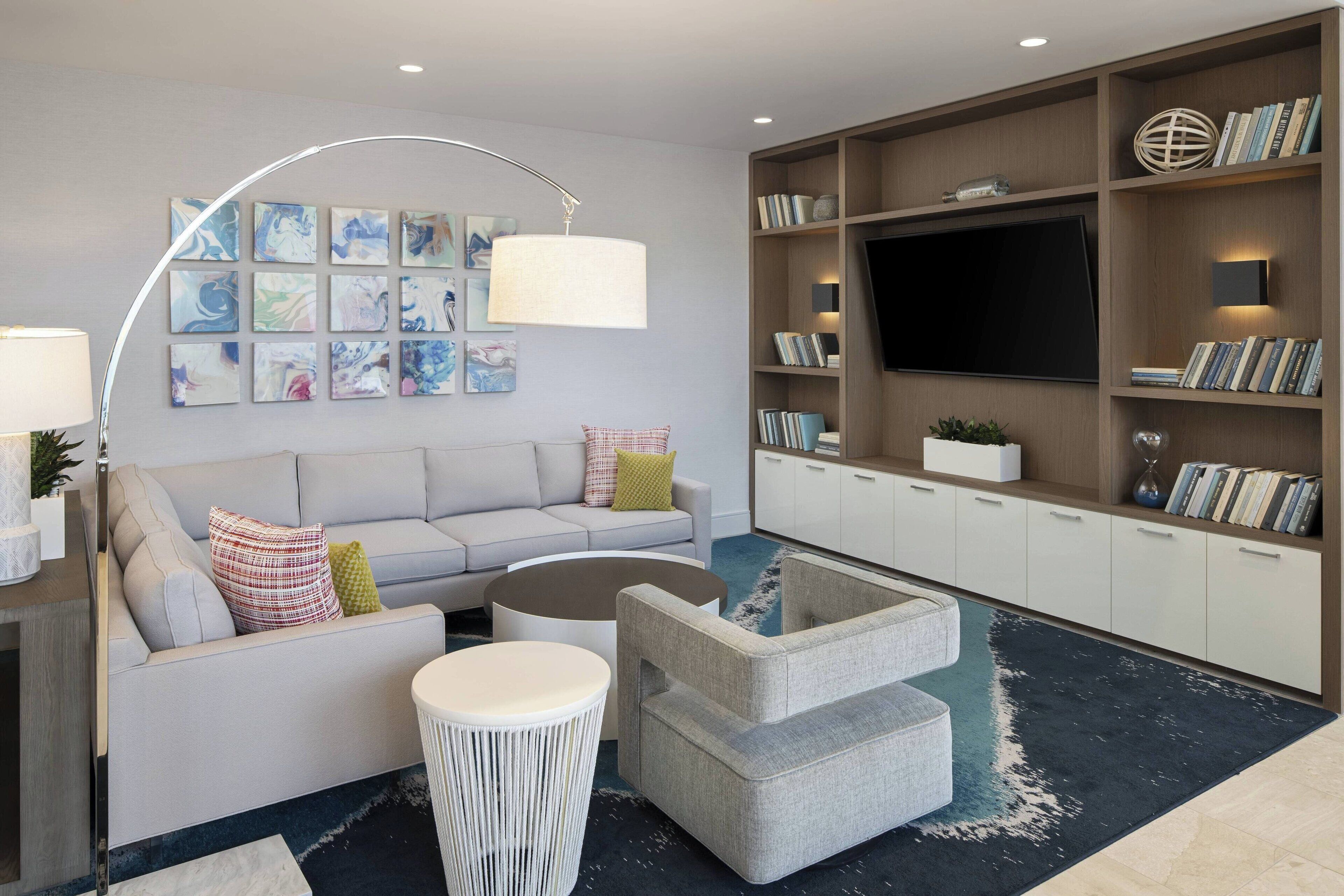 A modern living room with a sofa, coffee table, and armchairs, a bookshelf, and a flat-screen TV.