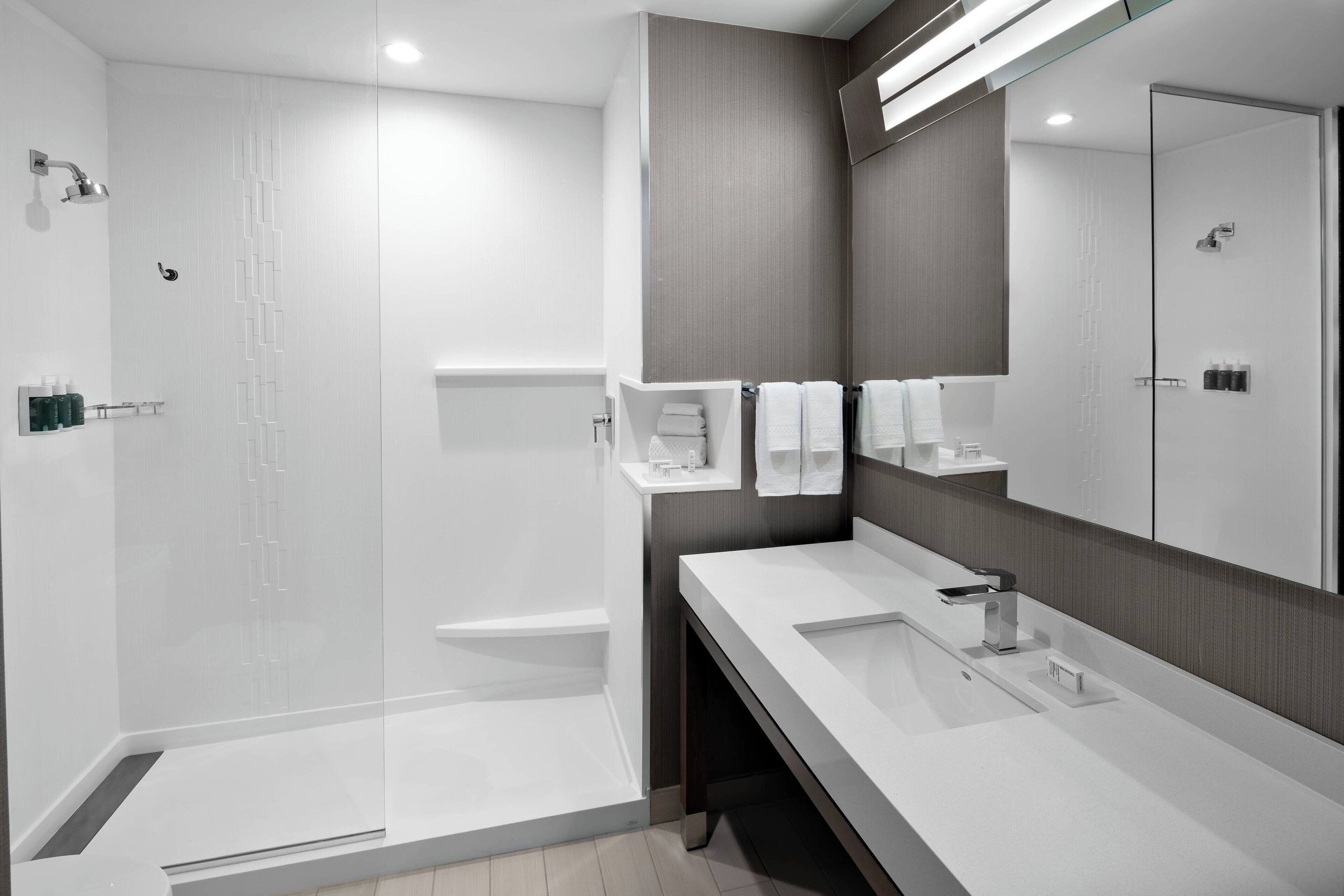 Un baño moderno con ducha de vidrio, un espejo grande y un mueble de tocador blanco.
