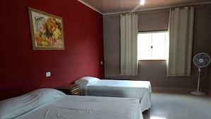 Habitación de hotel con dos camas, un cuadro en la pared, una ventana con cortinas y un ventilador de pie.