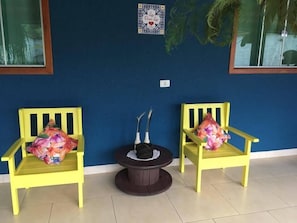 Dos sillas amarillas con cojines estampados, una mesita redonda y un adorno de pared.