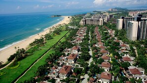A coastal residential area with beachfront properties, a golf course, and high-rise buildings in the background. - Amanda Seaview Resort Apartment (Lingshui)