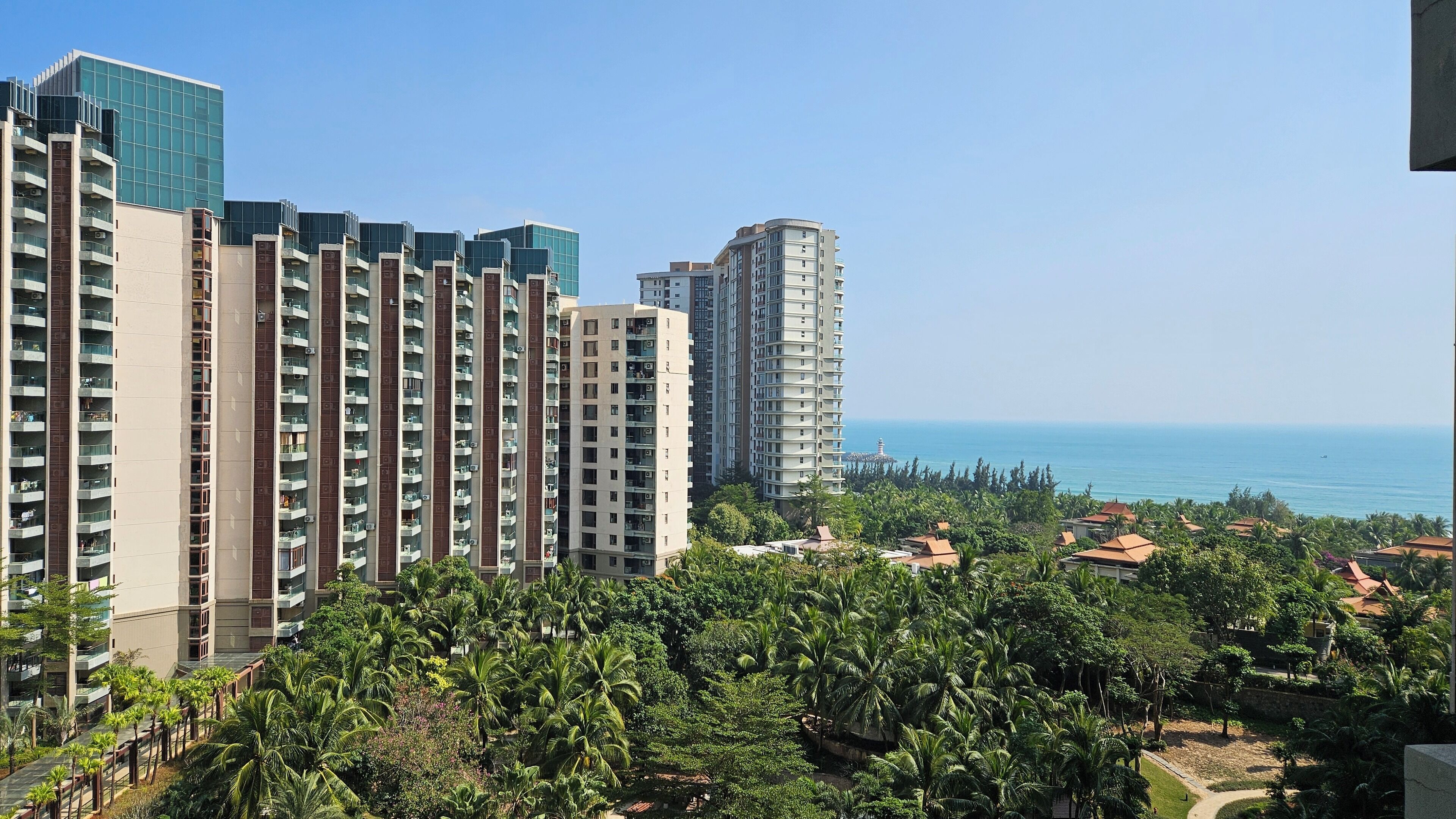 Un immeuble résidentiel de grande hauteur, doté de nombreux balcons, offrant une vue sur la mer et bordé d’une végétation luxuriante au premier plan.