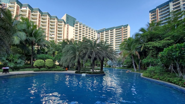 A swimming pool surrounded by lush greenery and tall buildings. - Amanda Seaview Resort Apartment (Lingshui)