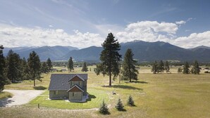 A house with a sloped roof, surrounded by a well-maintained lawn and several tall trees. - Bitterroot Oasis (Stevensville)