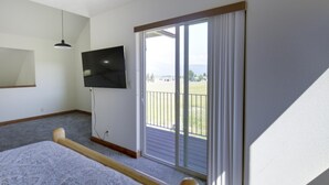 A bedroom with a large window, a flat-screen TV, a bed with a patterned bedspread, and a wooden headboard. - Bitterroot Oasis (Stevensville)