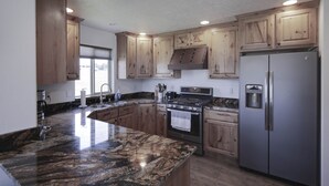 A kitchen with wooden cabinets, a granite countertop, stainless steel appliances, and a window providing natural light. - Bitterroot Oasis (Stevensville)