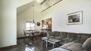 A spacious living area with a large gray sofa, a dining table with chairs, and a kitchen in the background. - Bitterroot Oasis (Stevensville)
