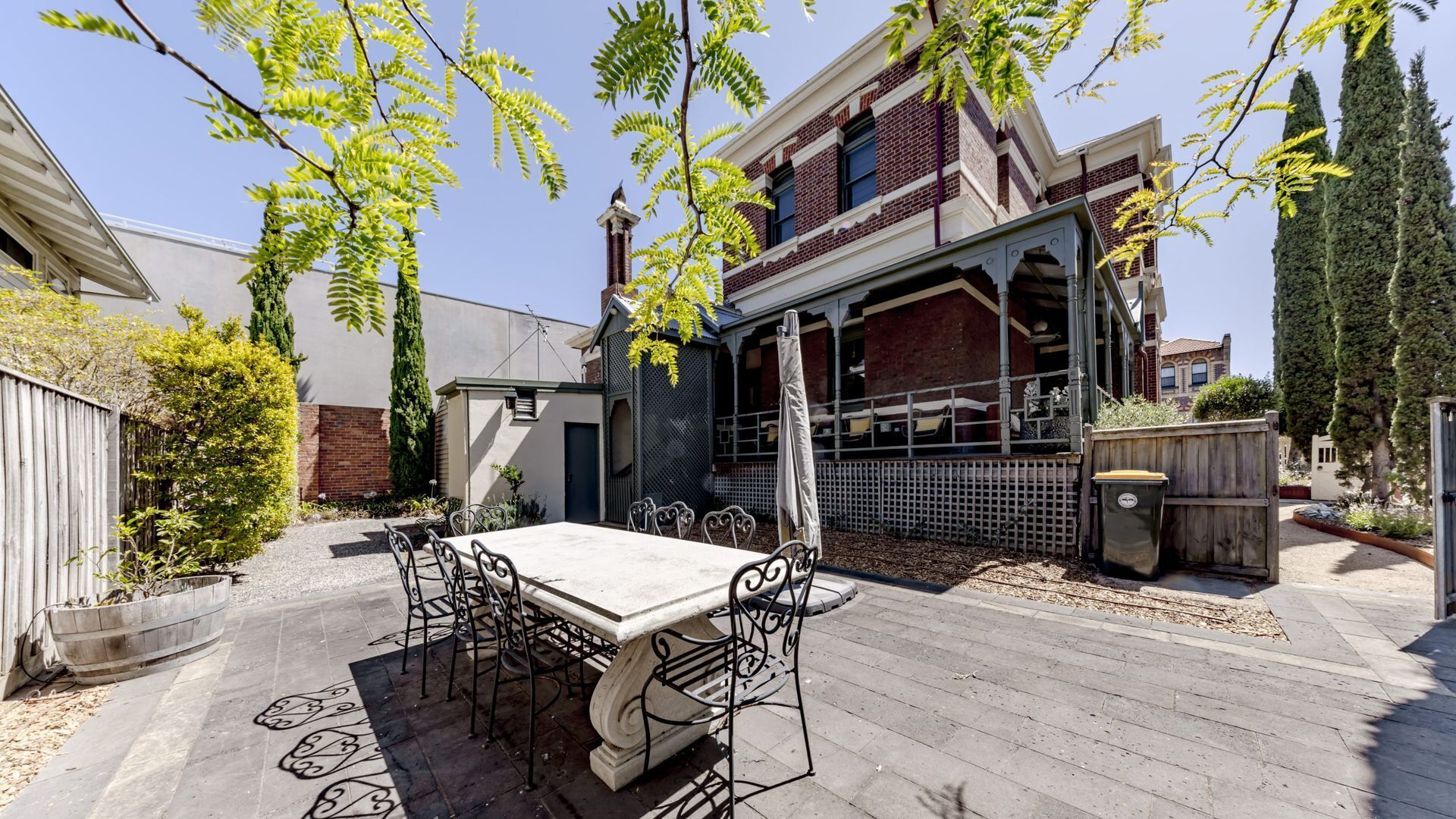 Eine Terrasse mit Tisch und Stühlen, eine Pergola und ein Backsteinhaus im Hintergrund.