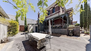 A patio with a table and chairs, a pergola, and a brick building in the background.