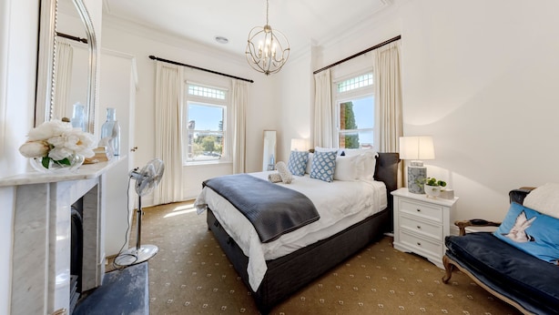 A bedroom with a bed, bedside tables, a mirror, a chandelier, and a window.