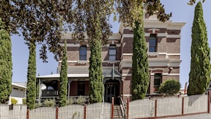 A Victorian-style building with a brick facade, multiple windows, and a white picket fence.