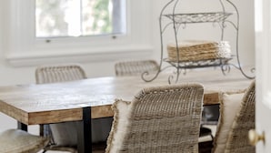 A wooden dining table with wicker chairs, a metal stand with baskets, and a window with natural light.