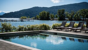 Una piscina cristalina con sillas de descanso y vistas a un lago y colinas boscosas.