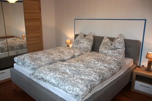Ein Doppelbett mit gemusterten Betttextilien, ein Nachttisch mit Lampe und ein Spiegel an der Wand.