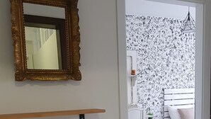 Ein Schlafzimmer mit einem Bett, einem Nachttisch, einem Sessel, einem kleinen Tisch, einer Wandablage, einem dekorativen Topf und einem Spiegel.
