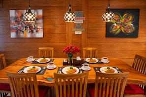 A wooden dining table with chairs, surrounded by paintings, and a sign with a coffee and wine message. - Mardika Private Villa (Ubud)
