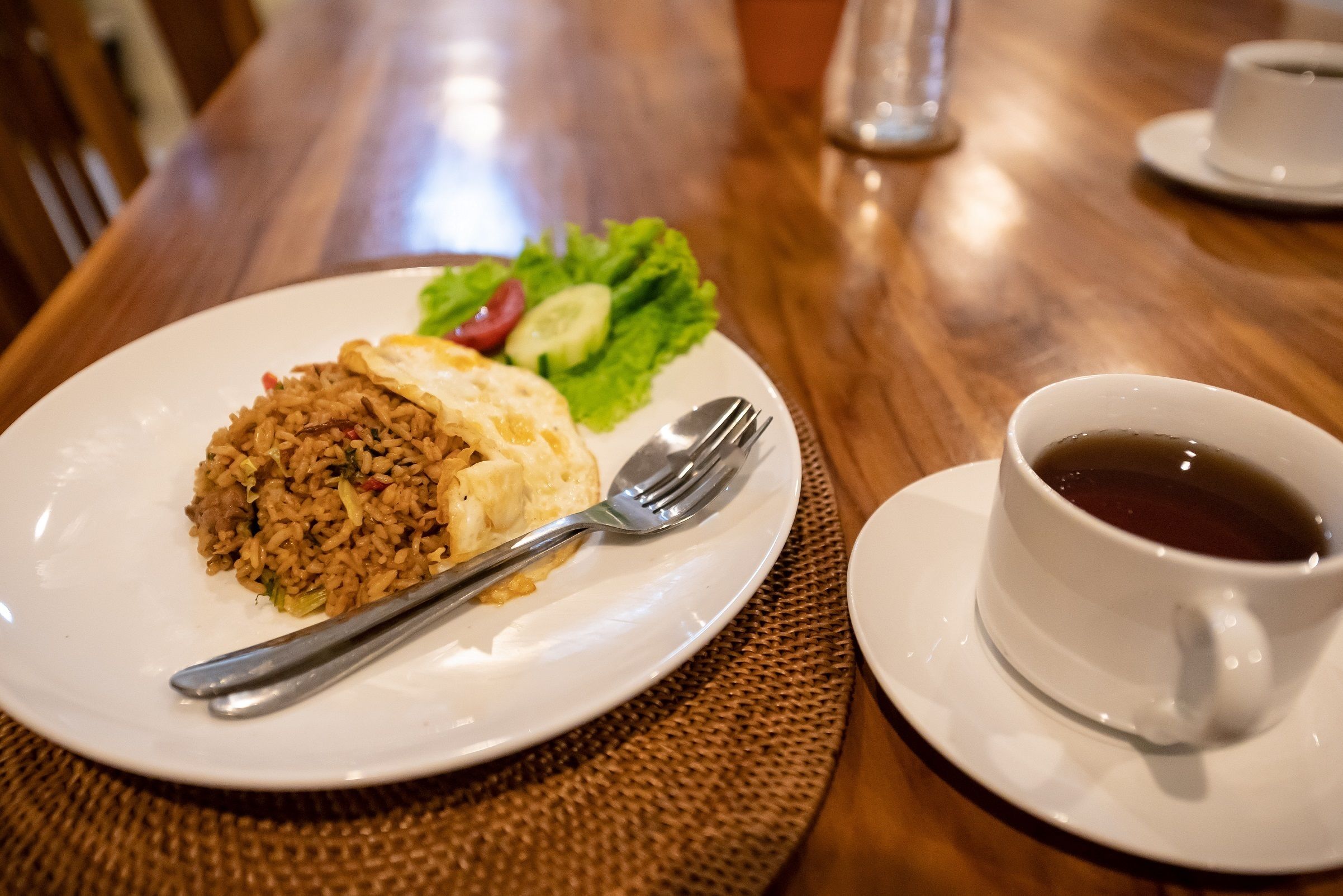 A plate of fried rice with vegetables and a cup of tea on a wooden table.