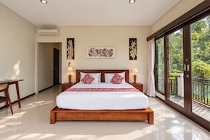 A spacious bedroom with a large bed, two bedside tables with lamps, a wooden headboard, and a large window with a view of greenery. - Mardika Private Villa (Ubud)