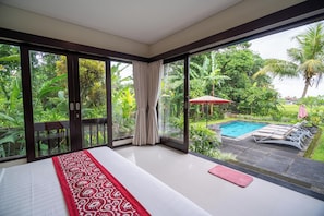 A bedroom with a large sliding glass door leading to a pool area, surrounded by lush greenery. - Mardika Private Villa (Ubud)