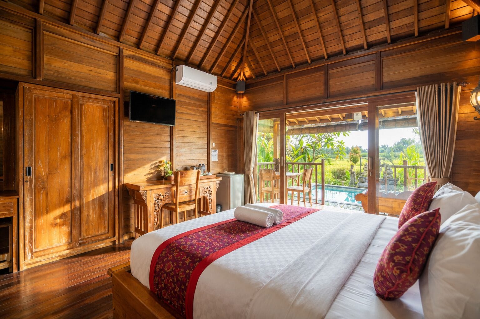A wooden room with a bed, a desk, and a view of a pool.