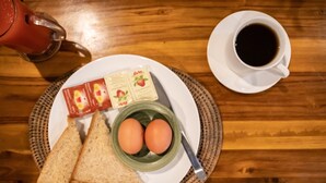 Un desayuno con tostadas, huevos, mermelada y café sobre una mesa de madera.