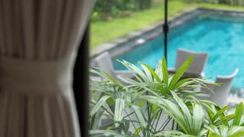 Vista de una piscina con sillas de descanso blancas y follaje verde al frente.