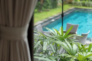 Vista de una piscina con sillas de descanso blancas y follaje verde al frente.