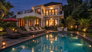 Uma casa de dois andares com piscina, área de estar externa e varanda bem iluminada.