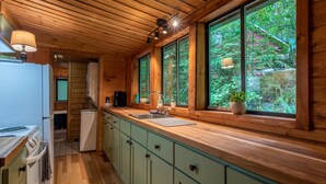 A kitchen with wooden cabinets, a sink, and a window overlooking a forest. - Cozy cabin in the Woods, Hot tub, secluded, walk to ZigZag River ! (Rhododendron)