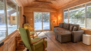 A cozy cabin interior with wooden walls, large windows, a sectional sofa, and a rocking chair. - Cozy cabin in the Woods, Hot tub, secluded, walk to ZigZag River ! (Rhododendron)