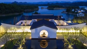 Un edificio tradicional japonés con un patio central, rodeado de árboles y vistas a un lago y montañas al fondo.