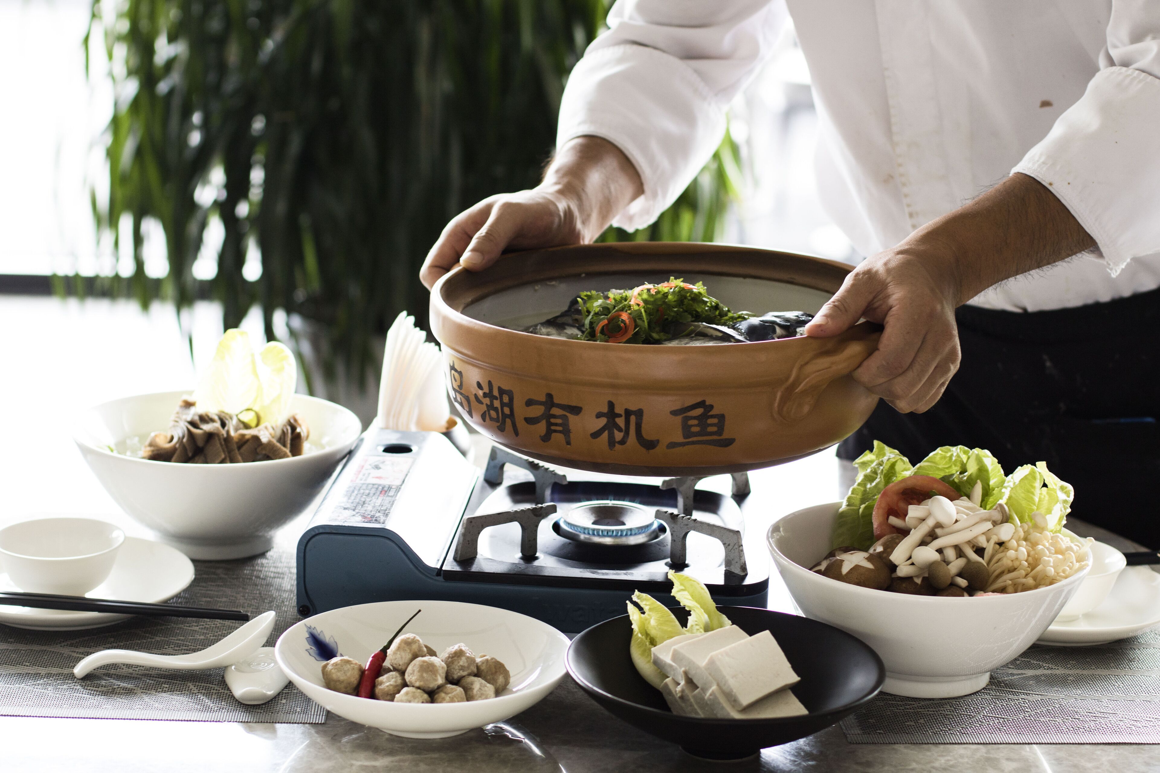 A dining setup with a hot pot, bowls of food, chopsticks, and a teapot.