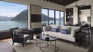 Una sala de estar moderna con un sofá, sillas y una mesa de centro, ventanas amplias con vistas a montañas y agua, y un ventilador de techo.