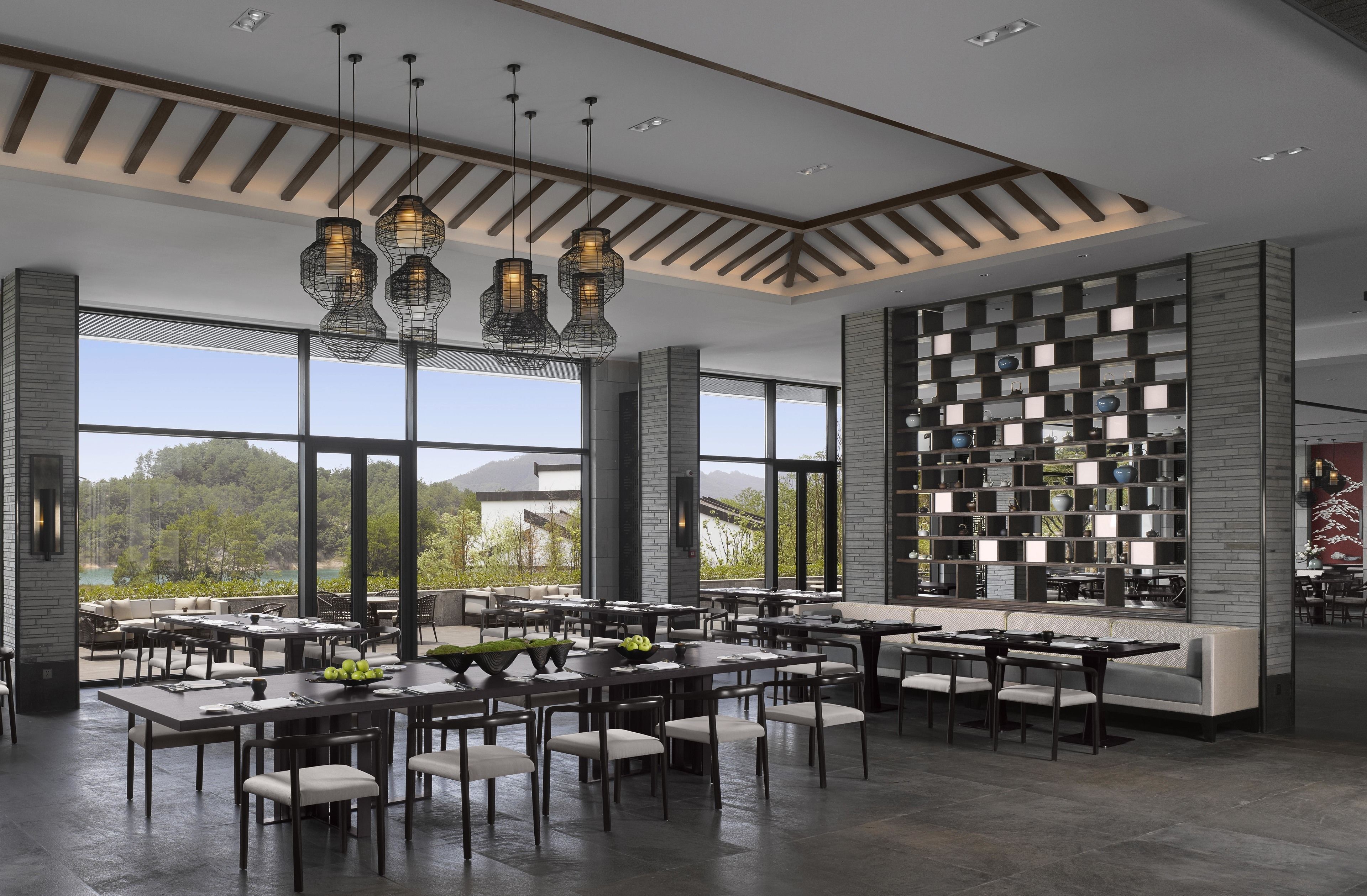 A modern dining area with multiple tables and chairs, large windows, and a decorative wall with shelves.