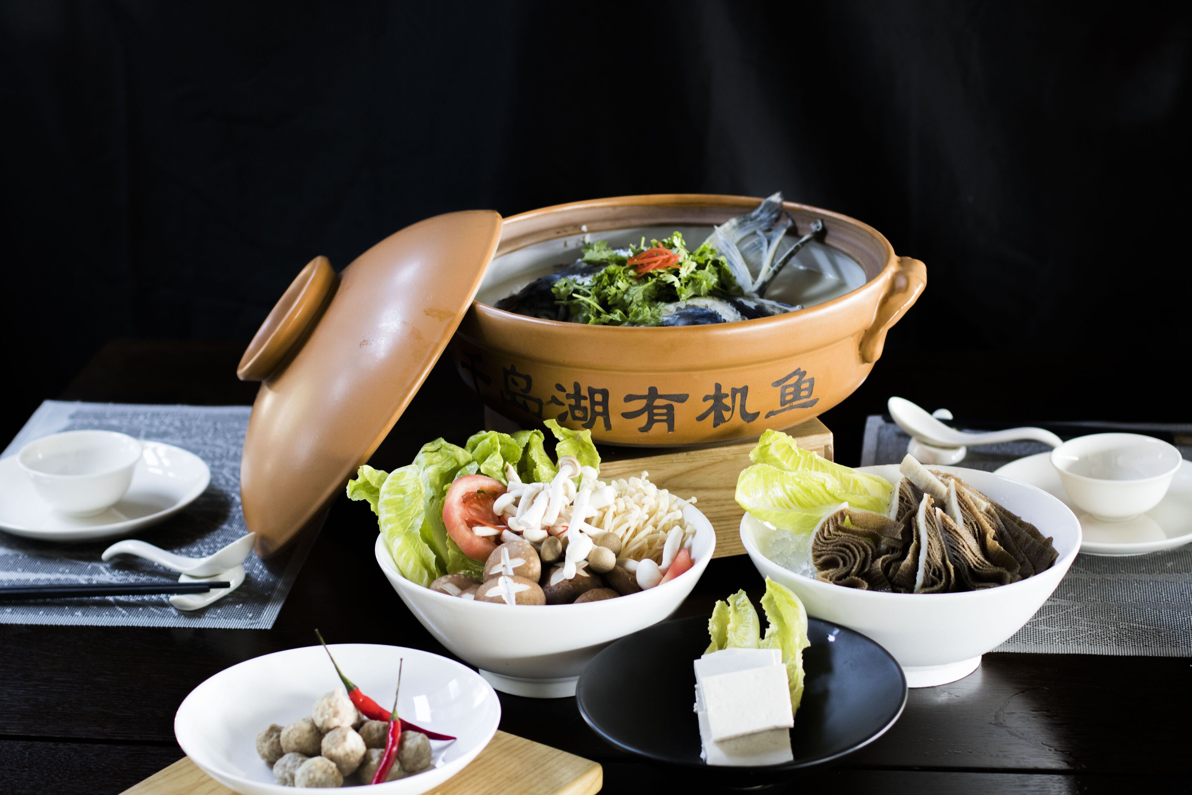 A traditional Chinese hot pot setup with a large clay pot, various side dishes, and a table setting.