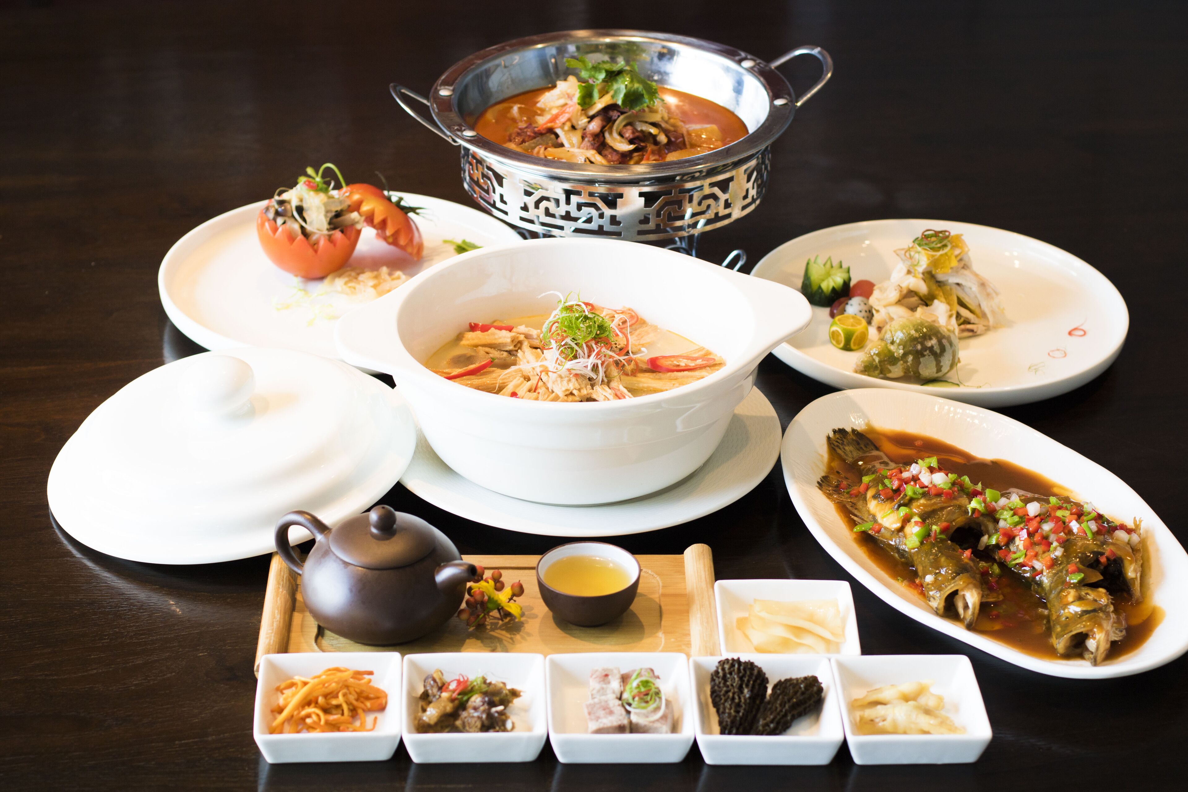 A variety of dishes on a table, including a bowl of soup, a fish dish, and several small bowls of condiments.