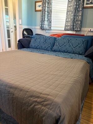 Un dormitorio con una cama grande, una silla y una ventana con cortinas estampadas.