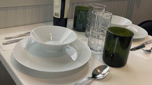 Une table dressée avec des assiettes blanches, une bouteille de vin, une tasse verte et des verres transparents.