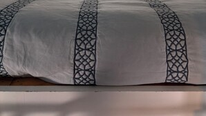 Une chambre avec un plafond en pente, deux oreillers blancs, un lit recouvert d’une couvre-lit à motifs et une fenêtre avec des rideaux.