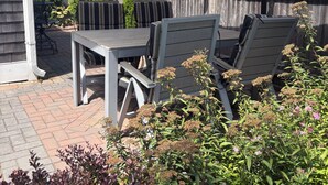 Une terrasse extérieure avec une table et des chaises sous un grand parasol, entourée de plantes en pot et d’une clôture en bois.