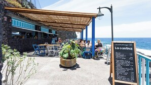 Un café en plein air avec des tables et des chaises, un tableau affichant le menu et une vue sur la mer.