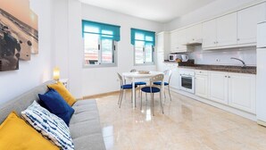 Une cuisine moderne avec des meubles blancs, une table à manger avec des chaises et un canapé avec des coussins.