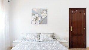 Une chambre à coucher avec un lit, une table de chevet, une porte en bois et une œuvre d’art représentant des fleurs, accrochée au mur.