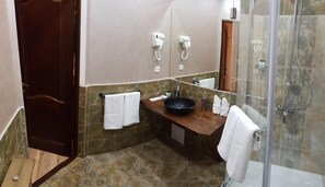 Une salle de bain avec un meuble-lavabo en bois, un lavabo noir, une cabine de douche en verre et un sol carrelé de marbre.