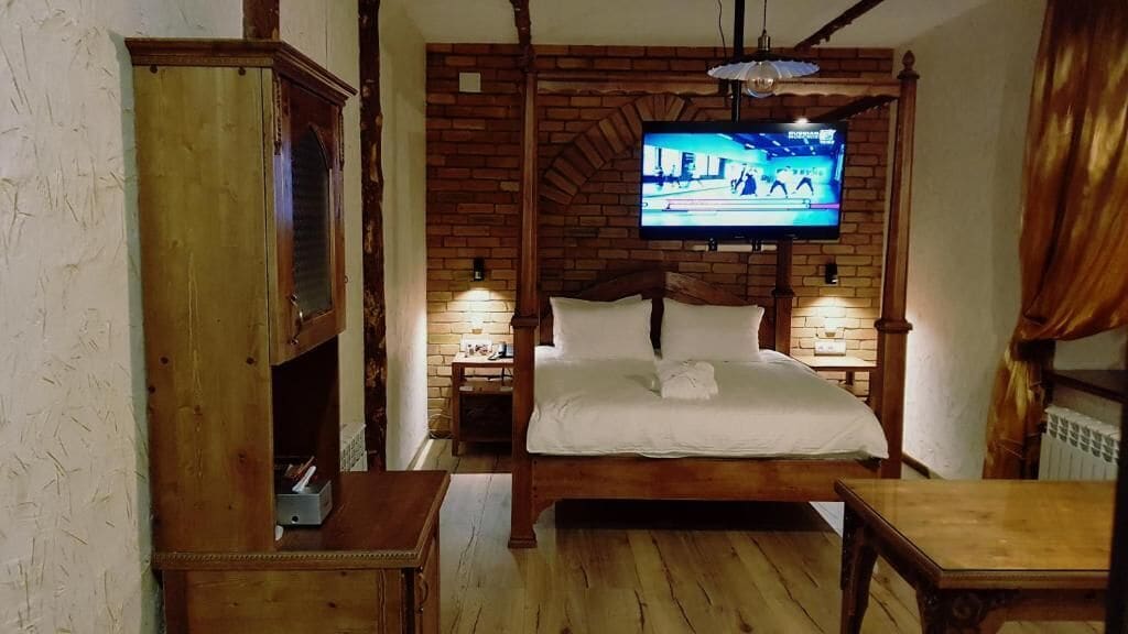 Une chambre à coucher avec un lit en bois, un téléviseur fixé au mur en briques et une armoire en bois.