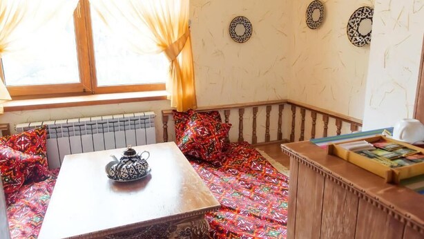 A cozy room with a wooden table, a bench with colorful cushions, and a radiator.