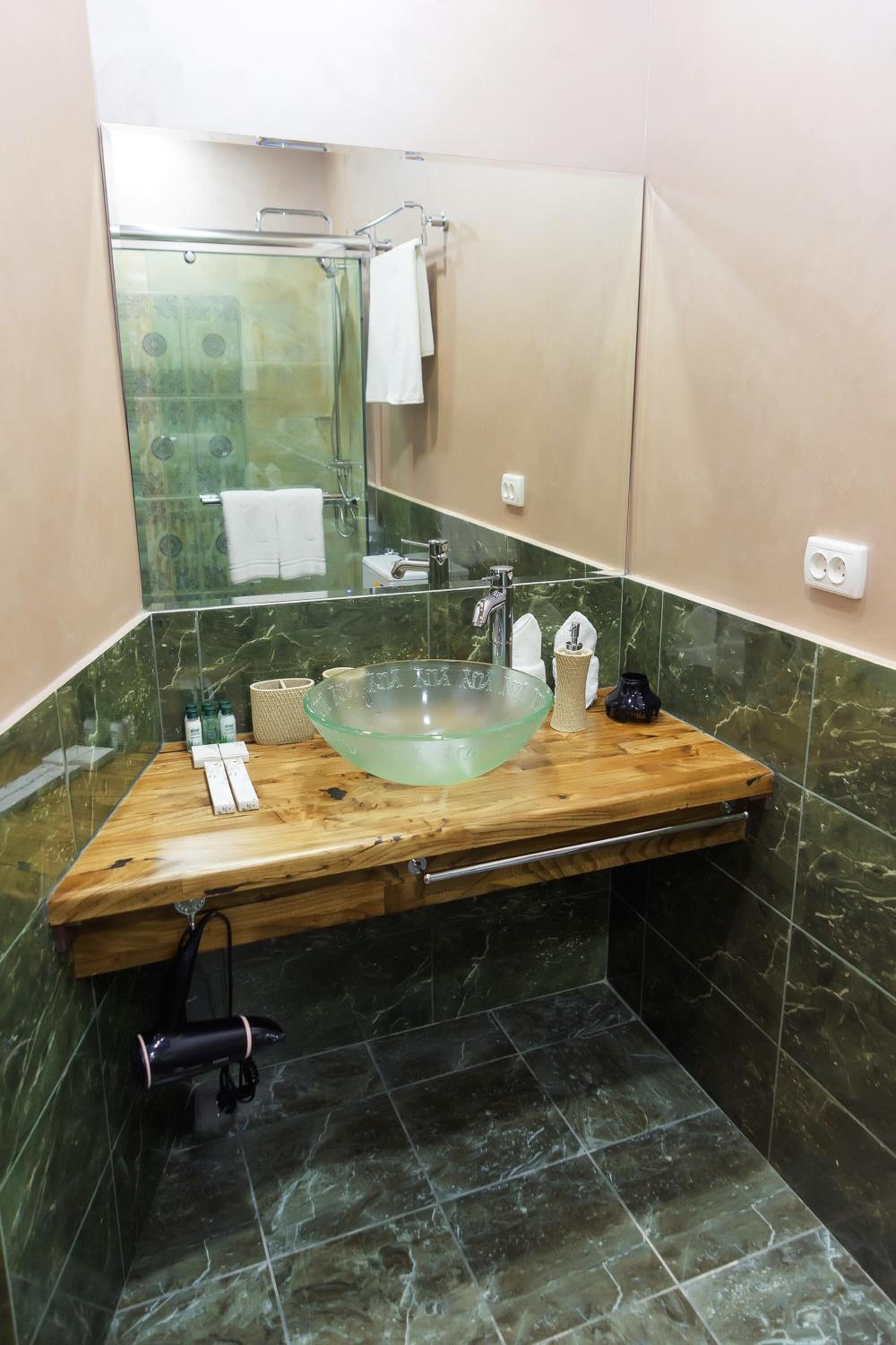 Een badkamer met een glazen wasbak, een houten aanrecht en een spiegel boven de wasbak.