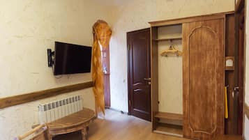 A room with a wooden wardrobe, a television mounted on the wall, and a radiator under a bench.