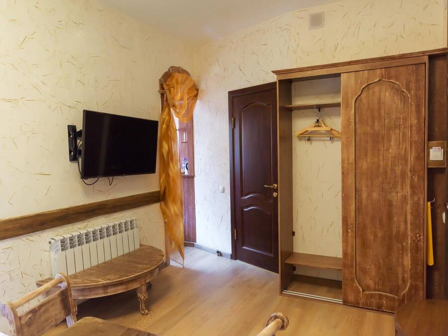 A room with a wooden wardrobe, a television mounted on the wall, and a radiator under a bench.