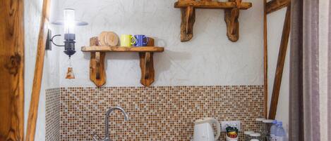 A kitchen with a wooden shelf holding mugs, a coffee maker, and a kettle.